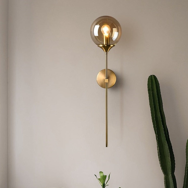 Amber glass globe wall light with brass finish and vertical spike design mounted on white wall - modern sconce lighting