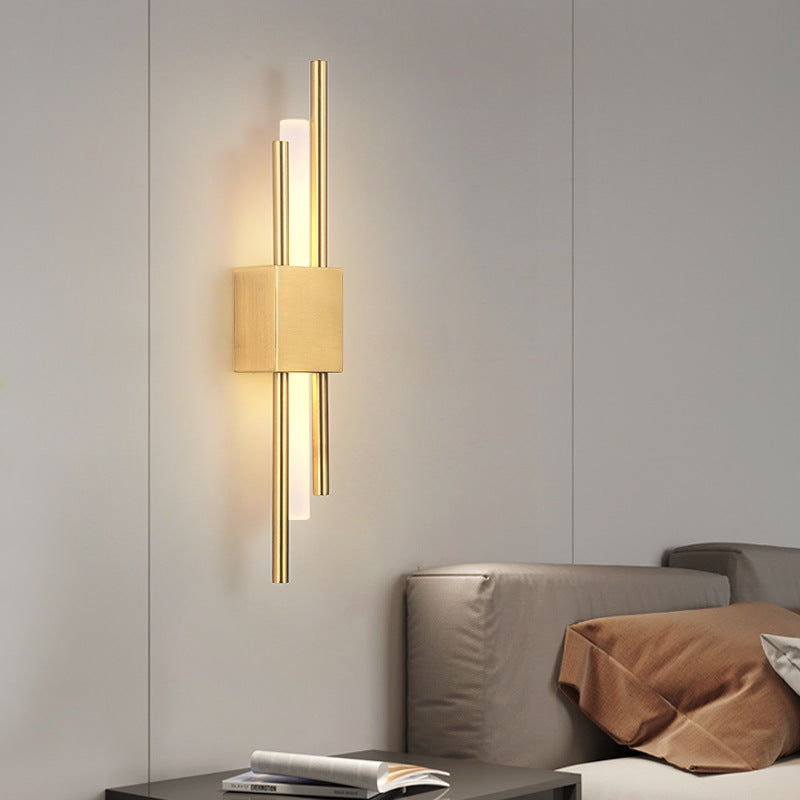 Modern gold brass LED wall sconce with cubic center mount and vertical rods emitting warm light on grey wall