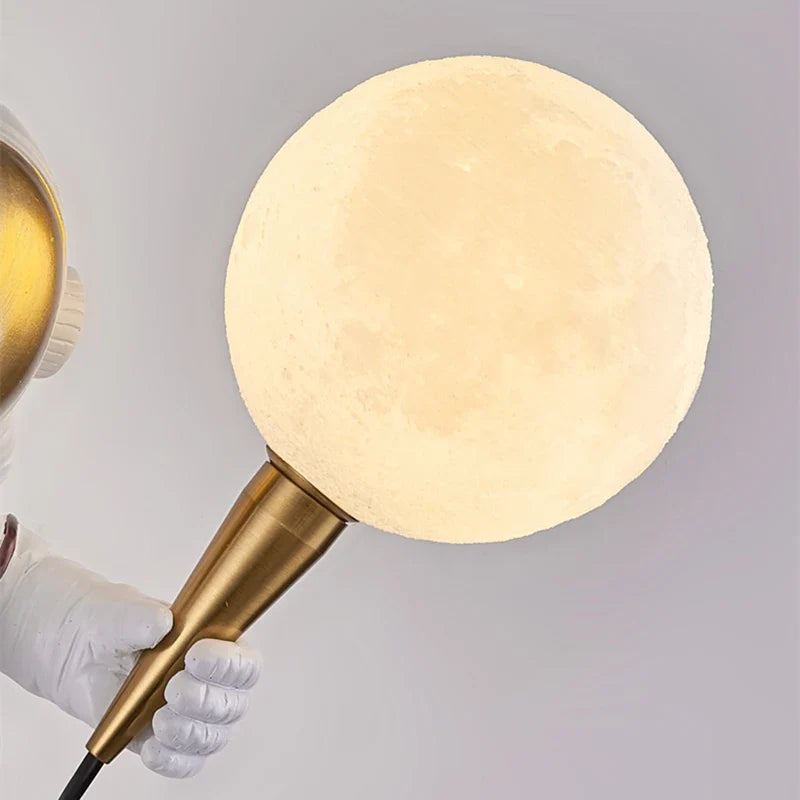 Gold brass astronaut wall light with warm white LED moon globe - close-up detail of metallic finish and glowing orb