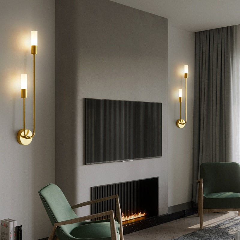 Modern brass LED wall lights with white tube shades in contemporary living room with fireplace and green chairs