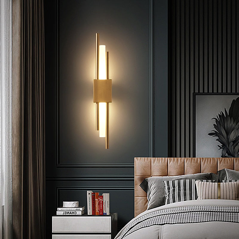 Golden brass LED wall sconce with vertical light bars mounted on dark green bedroom wall, modern geometric design