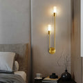Golden brass Spire LED wall light with dual cylindrical shades in modern bedroom setting, warm white glow, sleek design