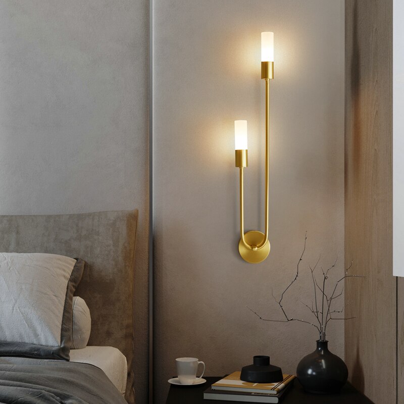 Golden brass Spire LED wall light with dual cylindrical shades in modern bedroom setting, warm white glow, sleek design