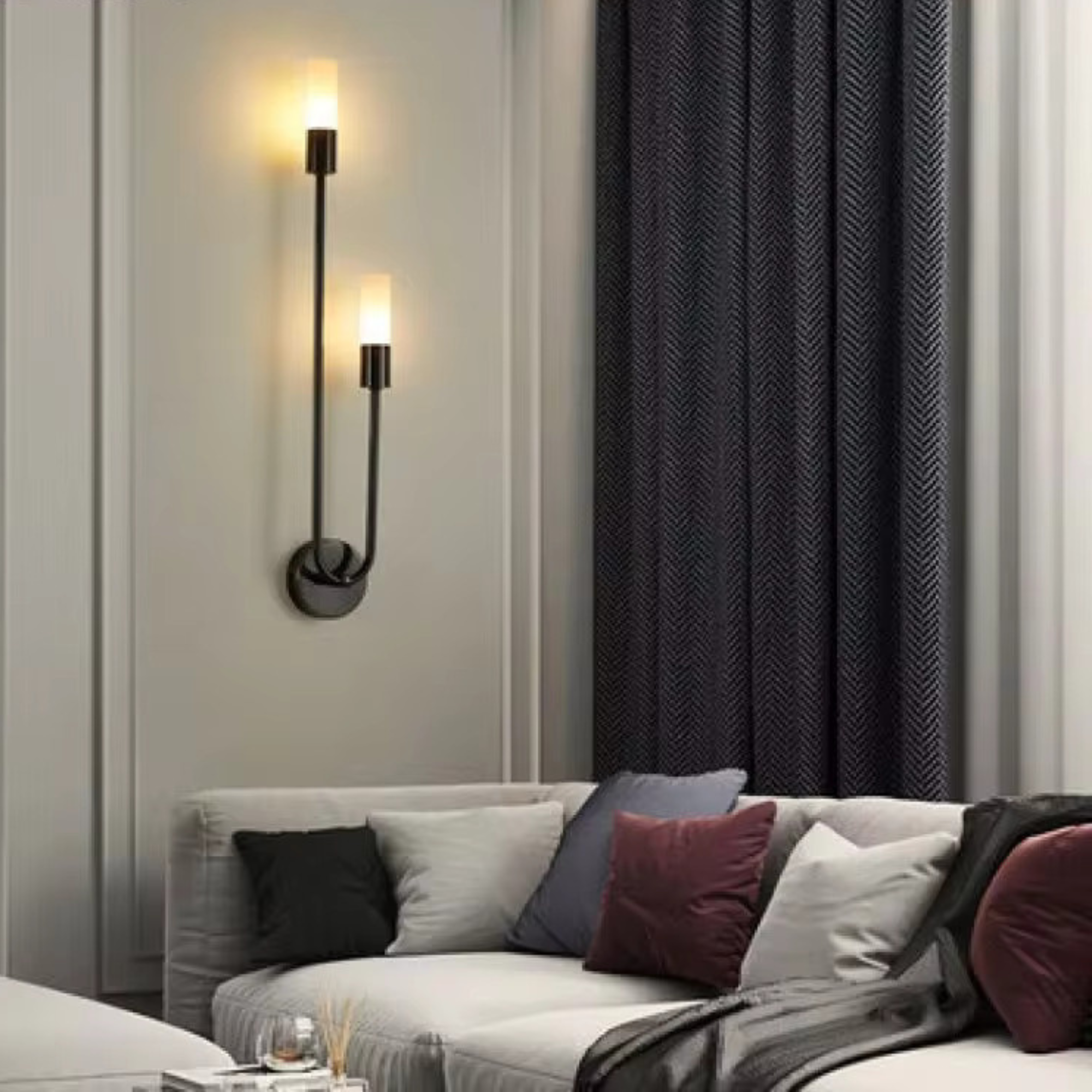 Black LED wall light with dual cylindrical shades mounted left on white wall above grey sofa with colorful cushions
